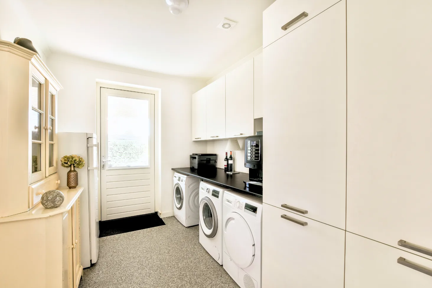 Custom white laundry room cabinets with built-in storage surrounding the washer and dryer
